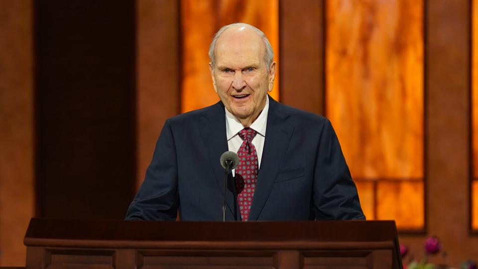 President Russell M. Nelson stands at a pulpit smiling at general conference for The Church of Jesus Christ of Latter-day Saints. 